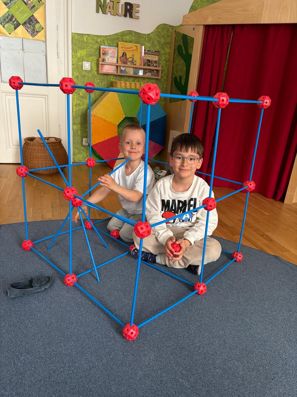 Zwei Kinder bauen mit blauen Stäben und roten Verbindungsstücken
