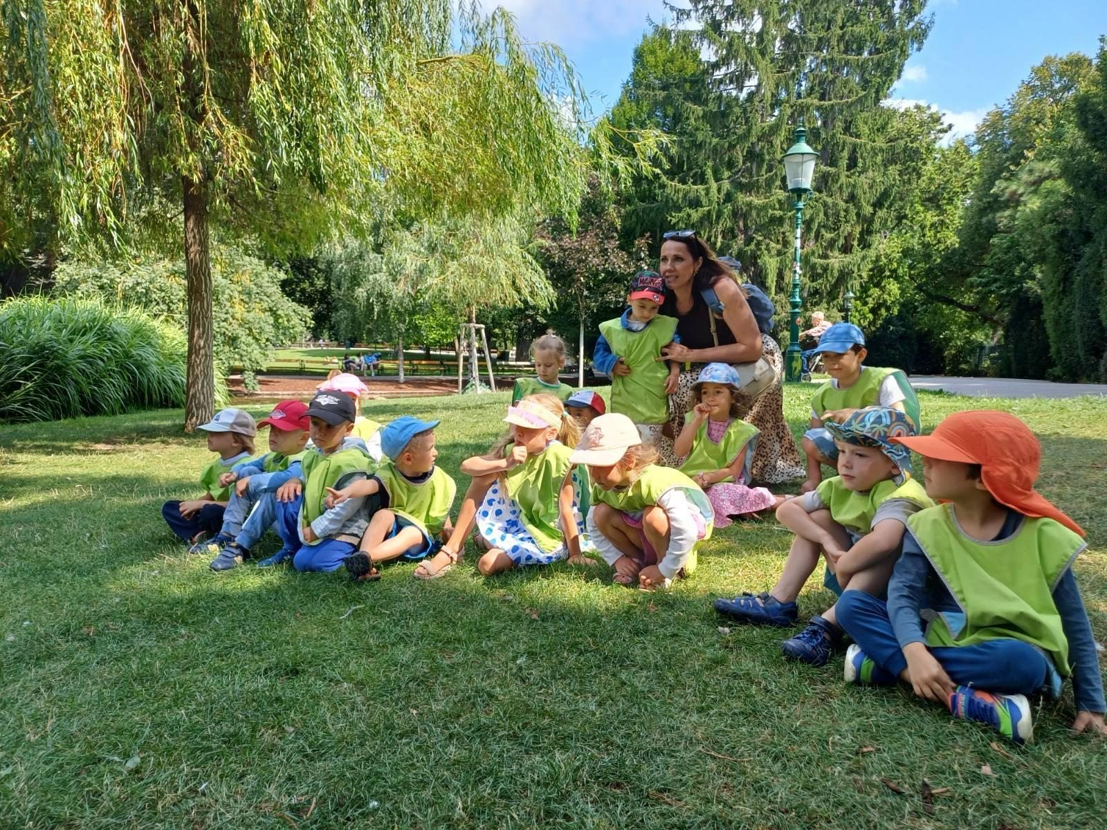Children and an accompanying adult sitting together on the grass in a park